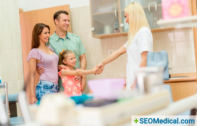 Female dentist shaking hands with young girl whose parents stand behind her